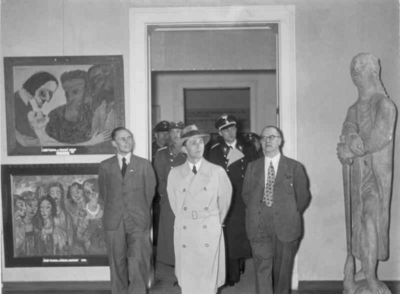 Goebbels auf der Ausstellung Entartete Kunst im Jahr 1938. Die beiden links hängenden Gemälde stammen von Emil Nolde: Christus und die Sünderin sowie Die klugen und die törichten Jungfrauen. Die Skulptur rechts ist Gerhard Marcks Heiliger Georg. Gerhard-Marcks-Heiliger-Georg-Goebbels-Ausstellung-Entartete-Kunst